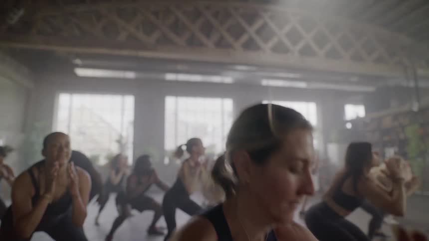 Women perform an energetic group fitness dance workout in a sunlit industrial studio