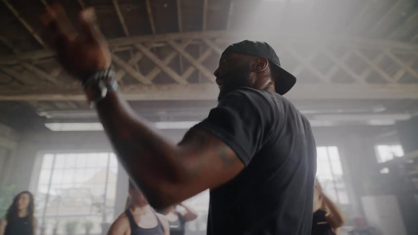 Slow motion shot of a male fitness coach inspiring his class as they clap and cheer in a hazy gym