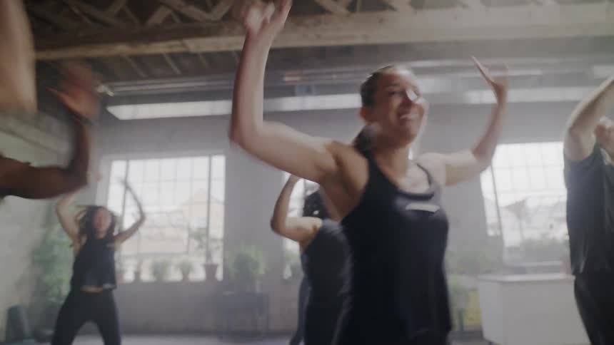 A diverse group of smiling people doing jumping jacks during a high-energy fitness class in a bright studio