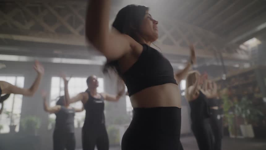 A motivated woman leads an energetic group through a high-intensity cardio workout with jumping jacks in a hazy fitness studio