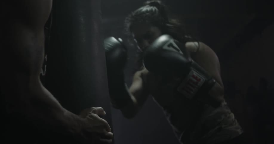 A woman punches a heavy bag as man helps