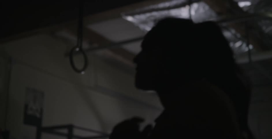 A woman shadow boxes jumping around a dark gym