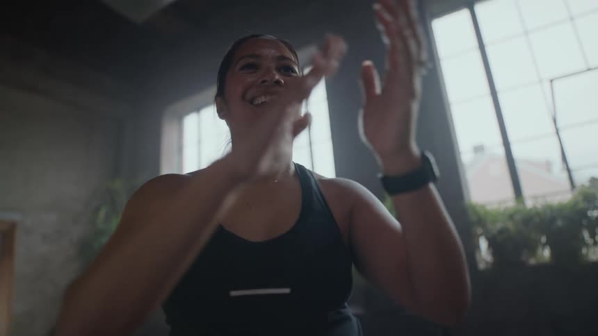 A smiling athletic woman celebrates a workout achievement by clapping enthusiastically in a modern industrial gym