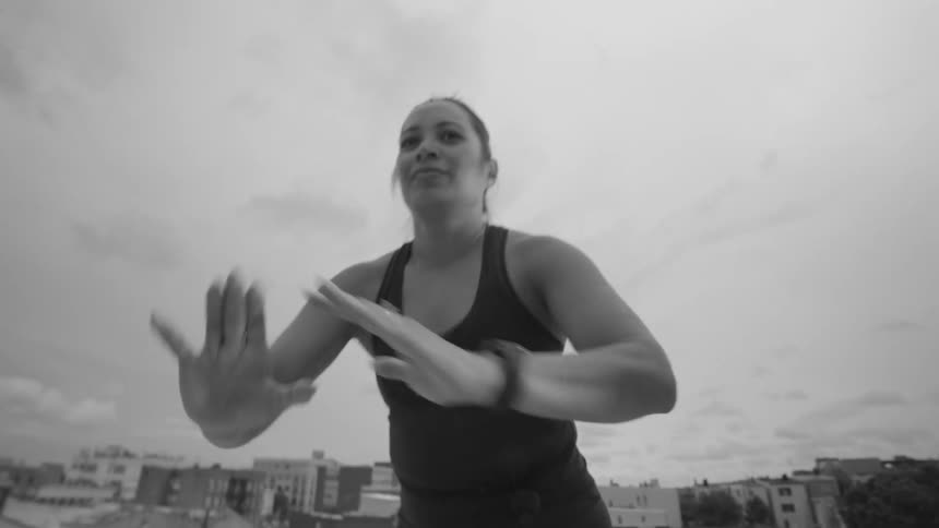 An athletic woman performs a slow, graceful martial arts routine on a city rooftop in dramatic black and white