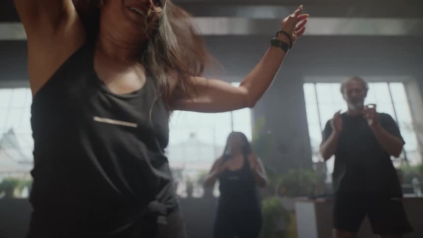 From a low angle, an energetic woman smiles and dances in slow motion during a lively group fitness class