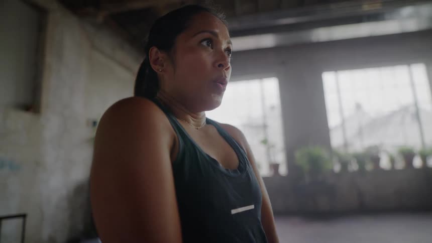 A determined woman catches her breath during an intense workout in a sunlit industrial gym