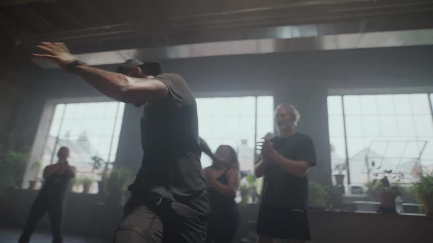 Slow motion shot of a powerful man performing an energetic and expressive dance routine in a hazy fitness studio while his class cheers him on