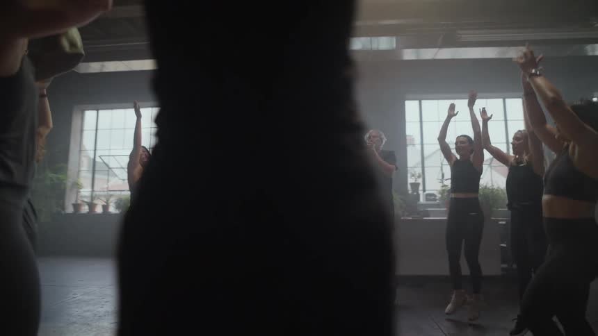 Slow motion pan of a diverse group of people doing jumping claps during a high-energy fitness class in a hazy studio