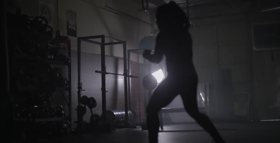 A woman spars and punches the air in a dark weight room