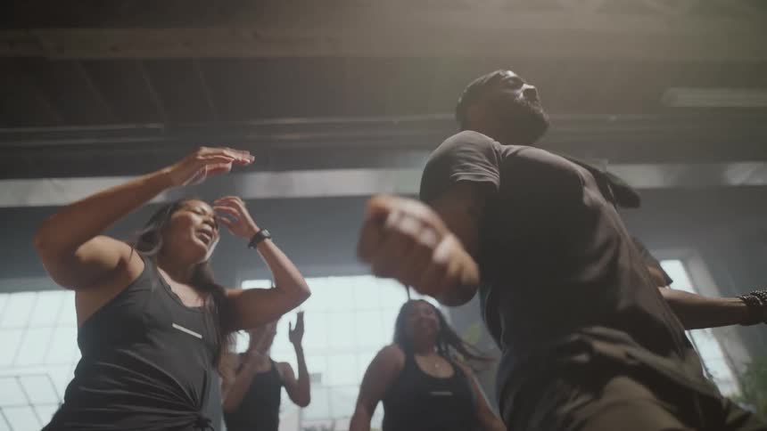 A diverse group of happy athletes dance and celebrate together in slow motion during a fitness class in a hazy gym