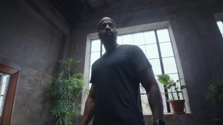 A powerful and determined athlete stands in a gritty, industrial gym with large windows before his workout