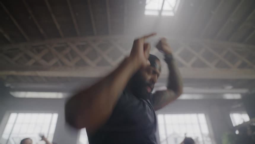 A passionate dance instructor with tattoos energetically leads a group class in a hazy, sunlit warehouse