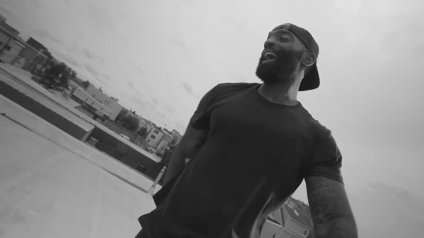 A smiling, athletic man stands up in slow motion after finishing a workout, filmed from a low angle in black and white