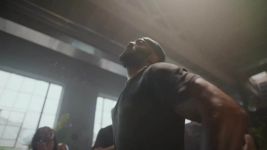 An athletic man dances with passion and energy in slow motion as a diverse group of people cheer him on in a sunlit loft