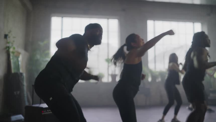 An energetic and diverse group of people smile while participating in a high-intensity cardio kickboxing workout in a studio