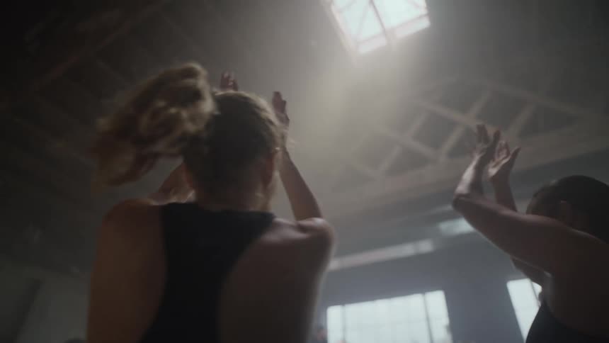 Slow motion shot of an athletic class clapping in unison, energized by the sunlight beaming into a hazy gym