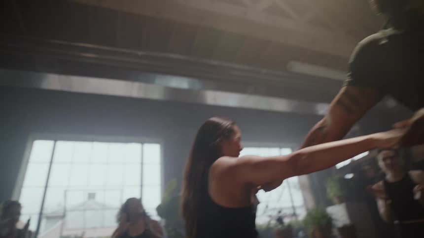 Slow motion shot of a joyful couple energetically dancing together in a sunlit studio as a group cheers them on