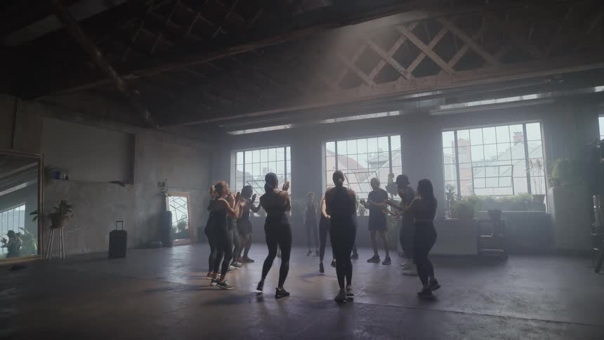 A group of friends cheer on a breakdancer in the middle of their dance circle in a sunlit industrial loft studio