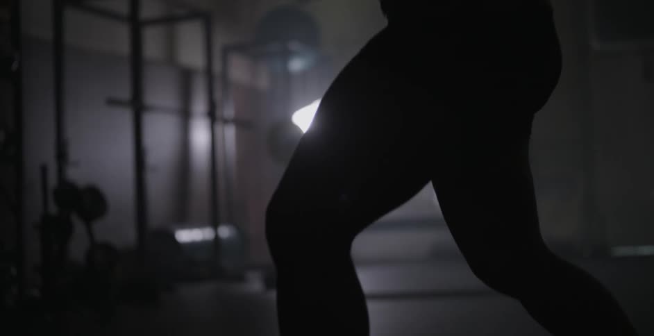 A woman is boxing and stepping around in a dark gym