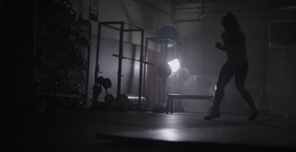A woman is shadow boxing by some weights in a gym