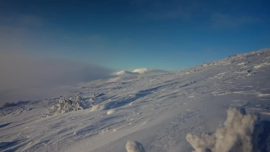 Expansive winter landscape of a snow-covered mountainside with fog rolling in below a clear blue sky