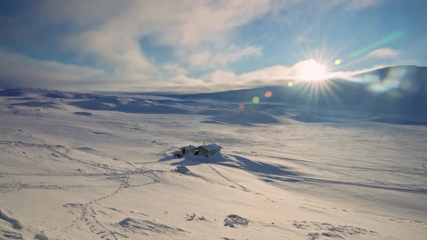The sun shines brightly over a remote cabin nestled in a vast, snow-covered landscape