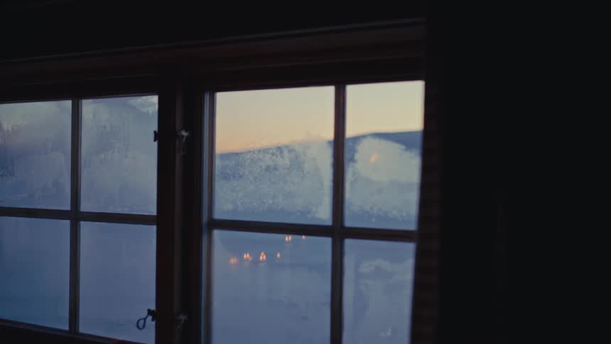 A serene sunrise over a snowy mountain landscape is revealed as the focus shifts through a frosted window