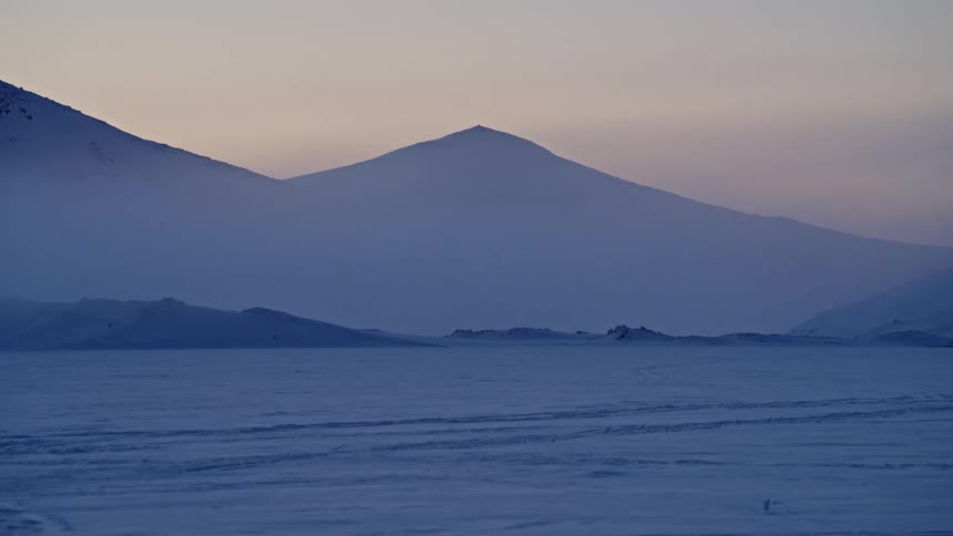 Timelapse of twilight fading over a vast, snow-covered mountain landscape during a cold, misty evening