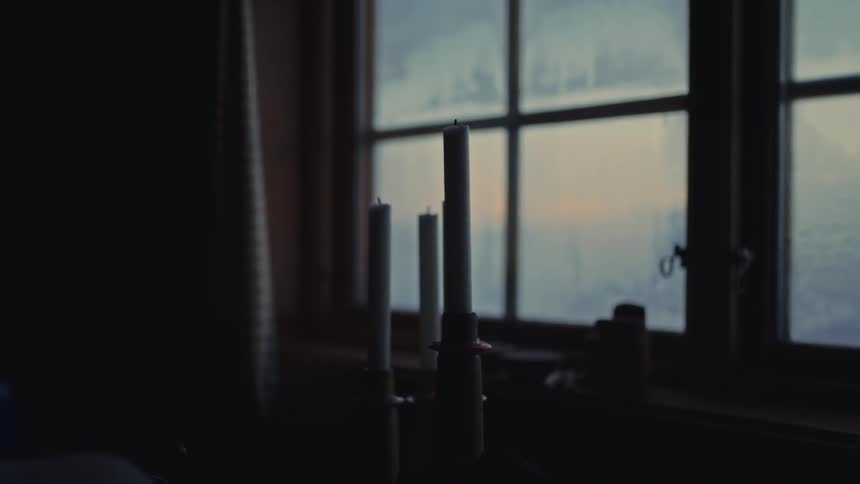 A moody shot of unlit candles on a windowsill as the focus shifts to the frosted glass on a cold evening