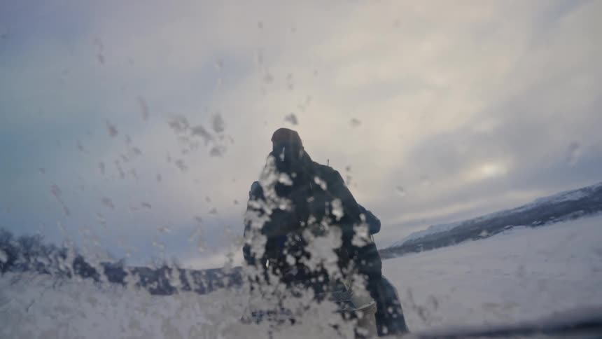 A cinemagraph shows snow spraying from the back of a snowmobile moving through a vast winter landscape