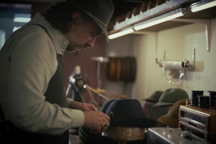 A skilled hatter meticulously adds the finishing touches to a handmade fedora in his traditional workshop