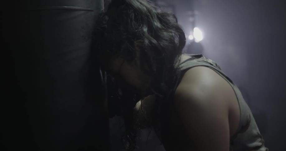 A woman breathes heavily while leaning against a punching bag