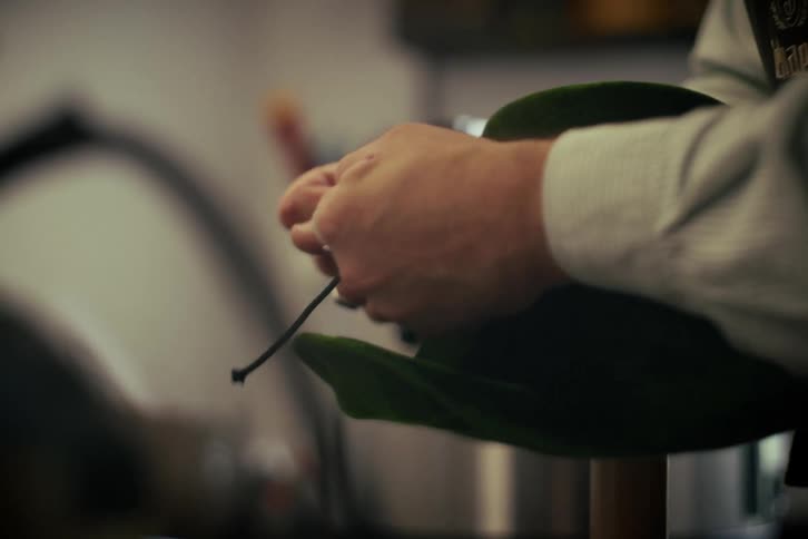 A close-up shot of a craftsman's hands meticulously threading a cord onto a green felt hat