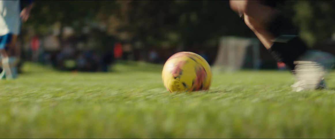 A young athlete dribbles a soccer ball down the field in slow motion before kicking it towards the goal