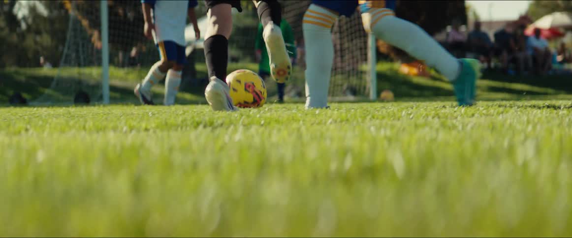 Energetic young boys compete in a soccer game on a sunny day, captured in a dynamic low-angle slow-motion shot