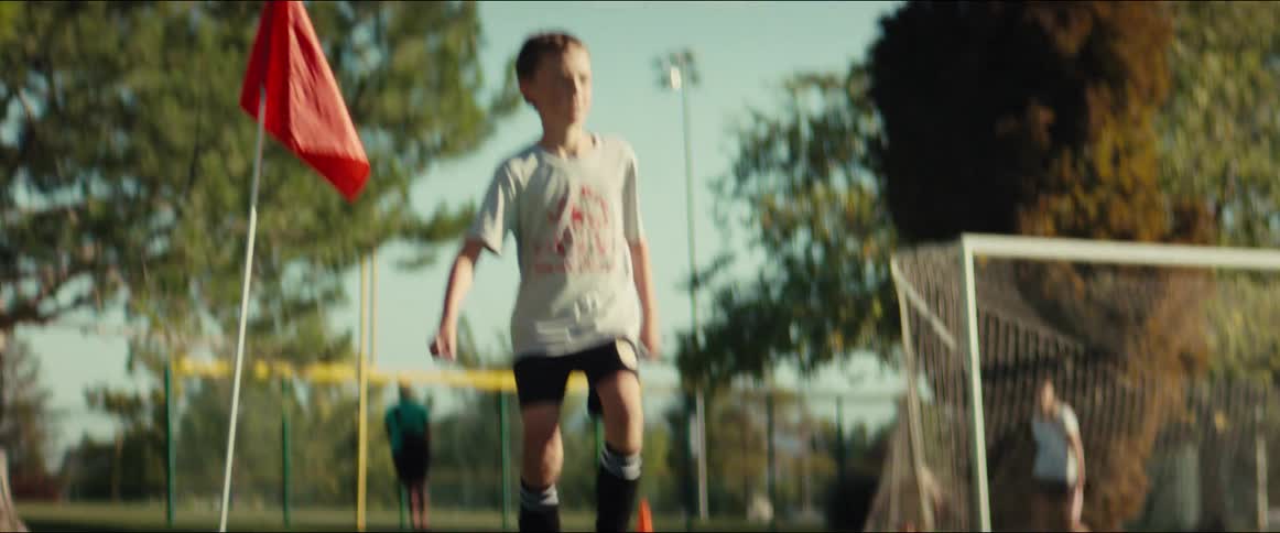 Cinematic slow motion shot from a low angle shows a young boy dribbling a soccer ball during practice on a sunny day