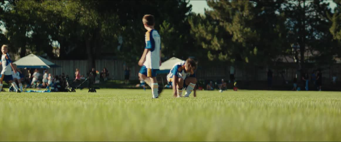 A young boy playing soccer falls down on the field, shakes off the apparent injury, and gets back into the game