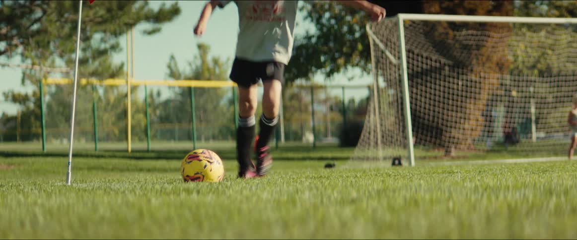 Dynamic low-angle shot of a young child kicking a soccer ball towards the goal on a grassy field