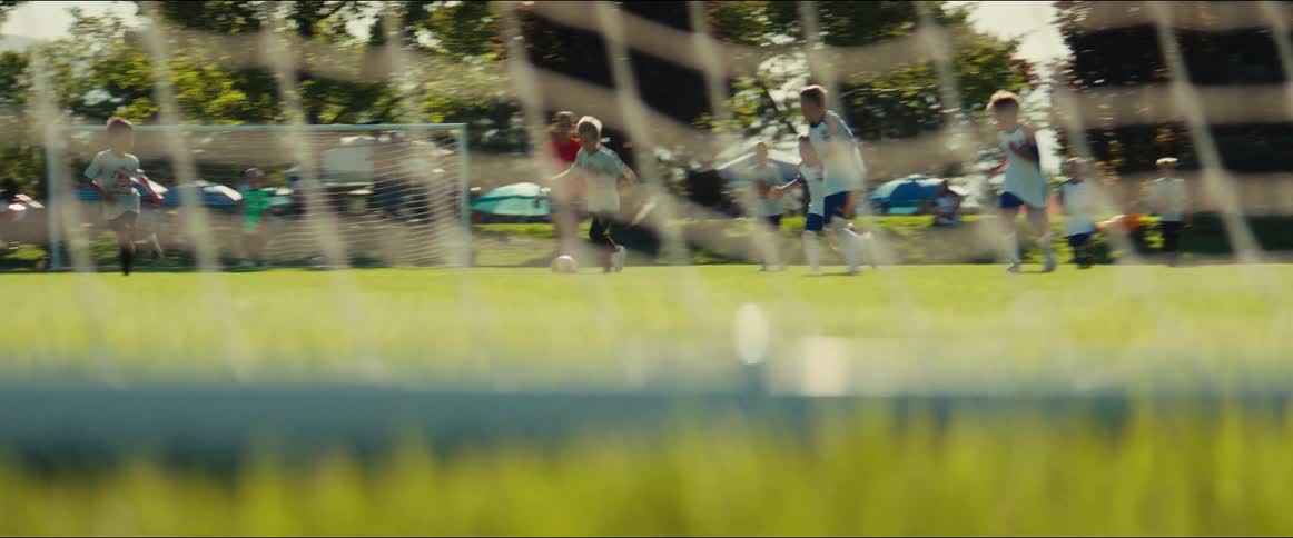 From behind the net, a young boy dribbles the soccer ball down the field during a game with his team