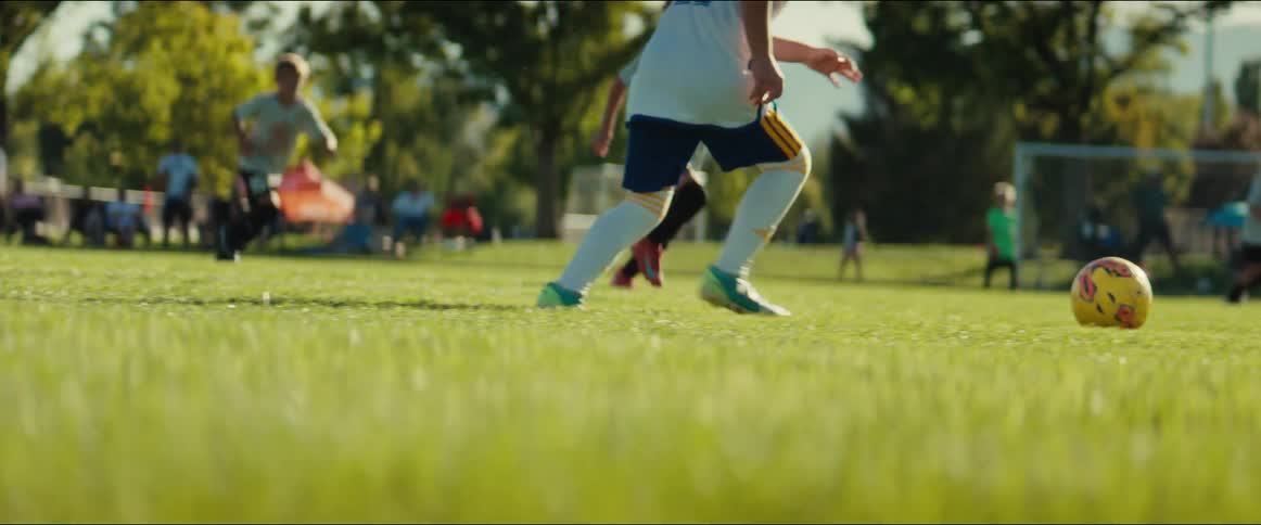 A young soccer player dribbles and kicks the ball down the field in a slow-motion, low-angle shot during a sunny outdoor game
