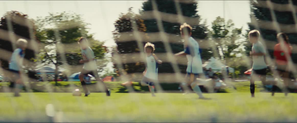 Energetic young soccer players run down the field during a game, filmed in dynamic slow motion from behind the goal net