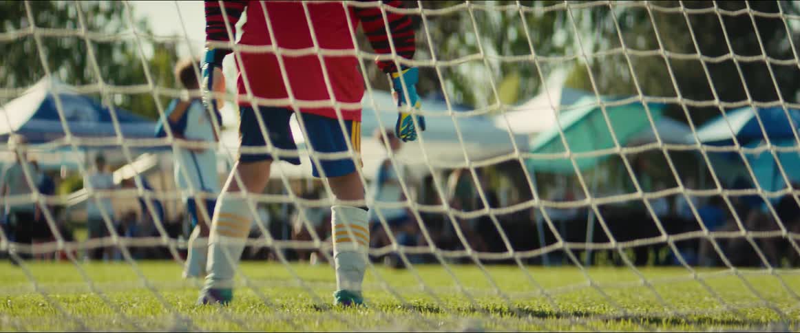 A young soccer goalie stands guard from behind the net during a competitive youth game on a sunny day