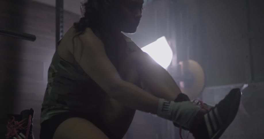 A female fighter is sitting in a gym tying her shoes