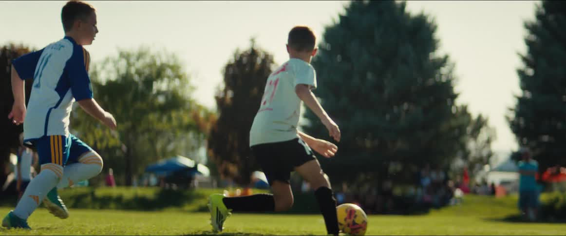 Low-angle slow motion shot of a young boy outmaneuvering a defender as he dribbles a soccer ball down the field during a game