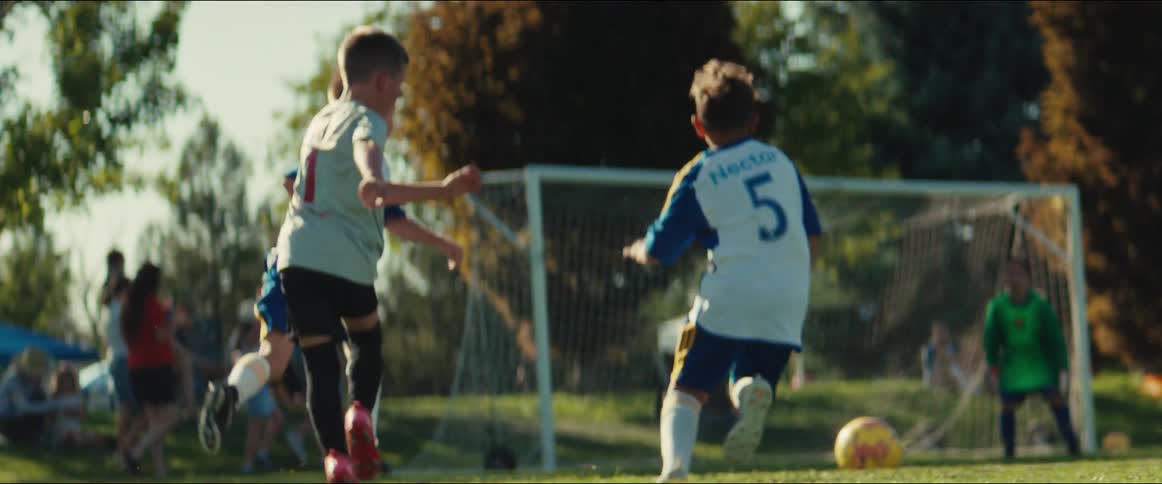 Slow motion shot of children playing in a soccer game as one player shoots and the goalkeeper makes the save