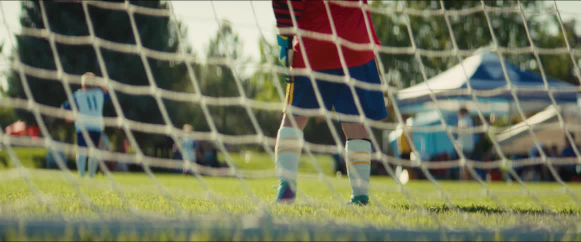 View from behind the net of a young soccer goalkeeper standing guard during a sunny day game