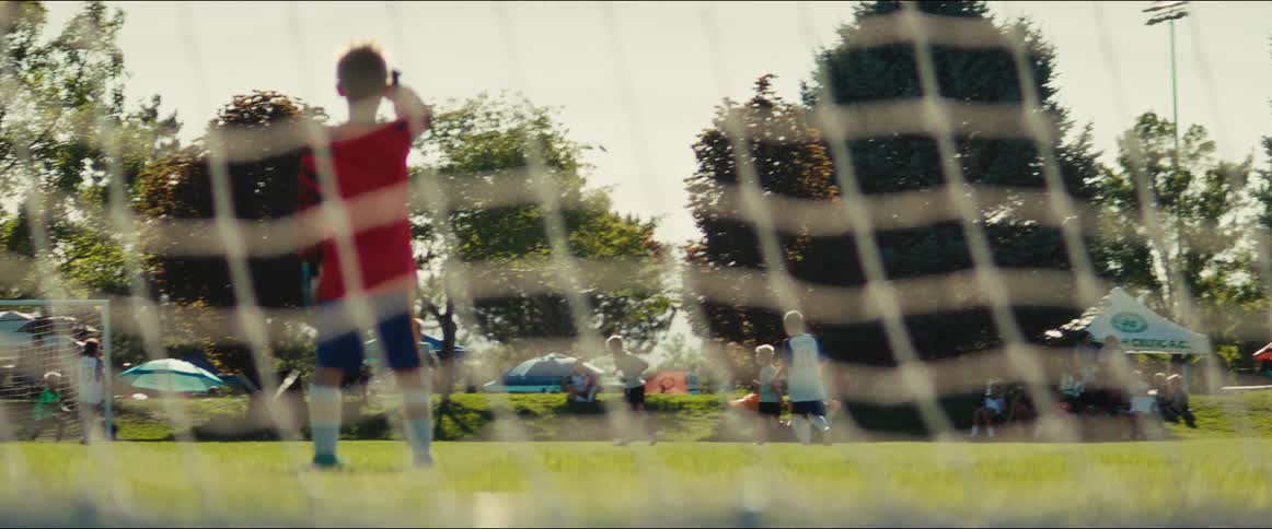 View through the soccer net of a young goalie in slow motion watching his team play a game on a bright sunny day