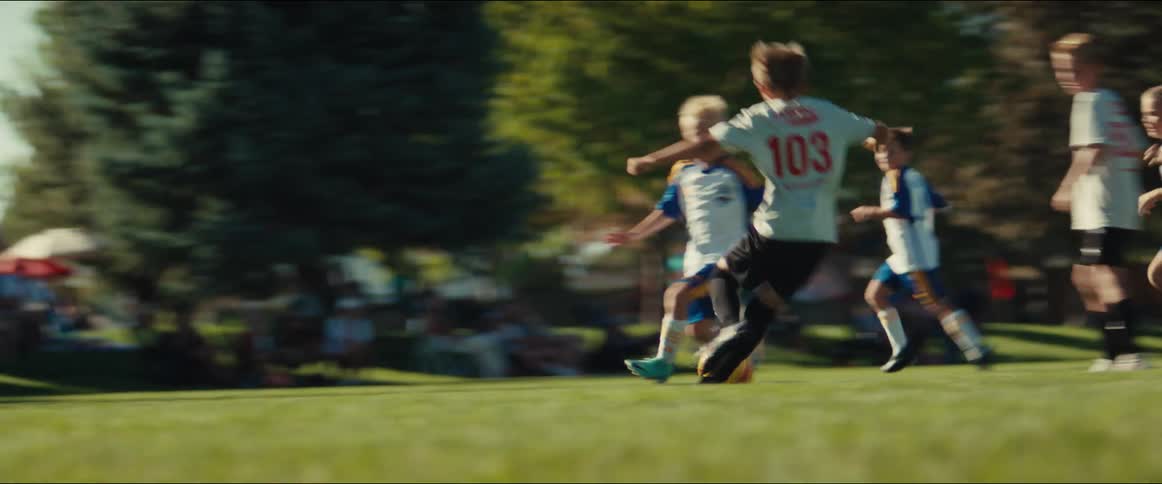 Slow motion shot of young boys running and chasing the ball during a competitive soccer game on a sunny day