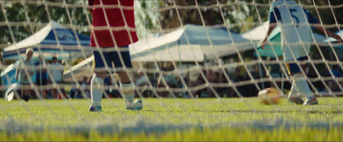 A young soccer goalie watches from behind the net as another player kicks the ball and scores a goal during a youth league match