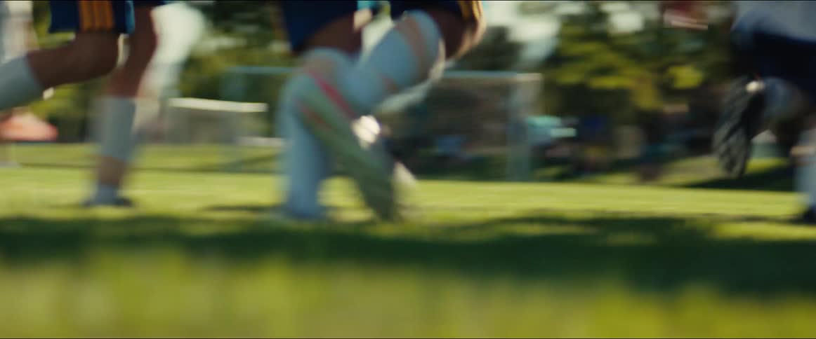 An energetic youth soccer team runs in slow motion across a sunny field, celebrating with high-fives